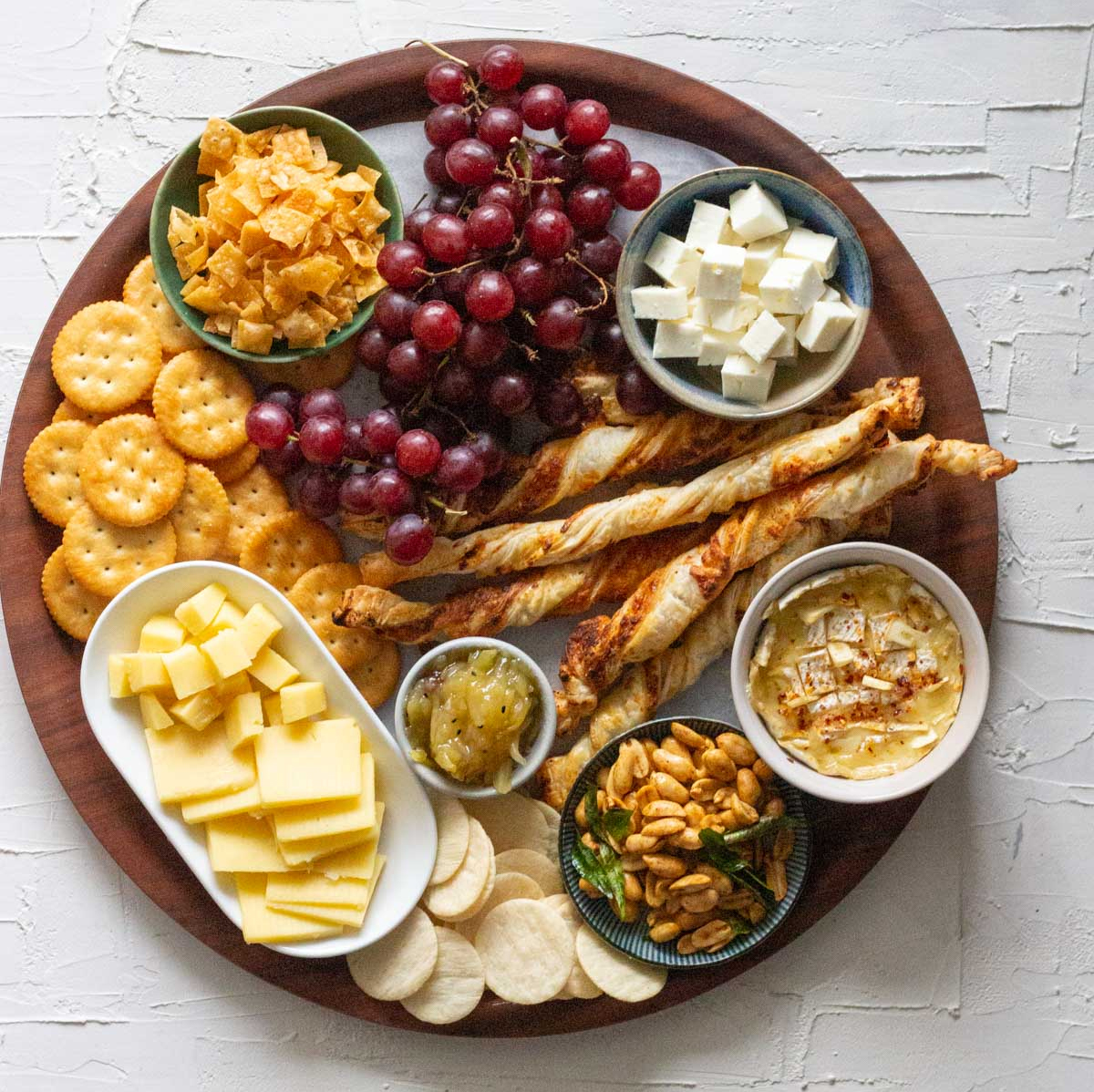 Mirchi Tales presents a cheese board with grapes, cheeses, and breadsticks.