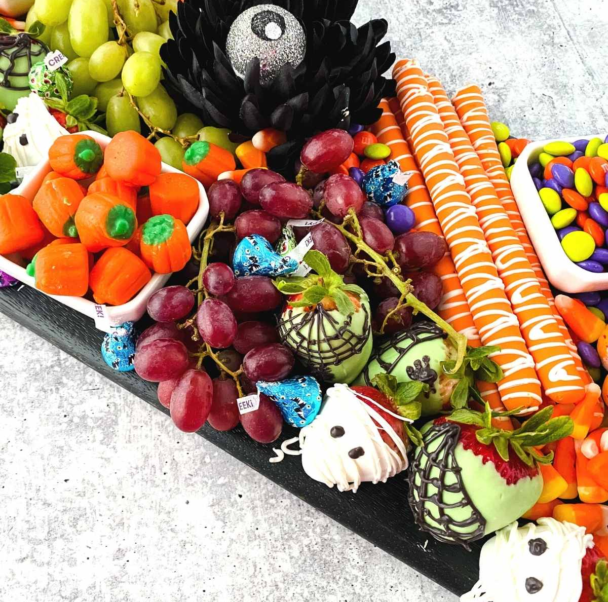 M&Ms, chocolate-covered pretzel sticks, and pumpkin candies are presented on A Re-Invented Mom's Halloween charcuterie board.