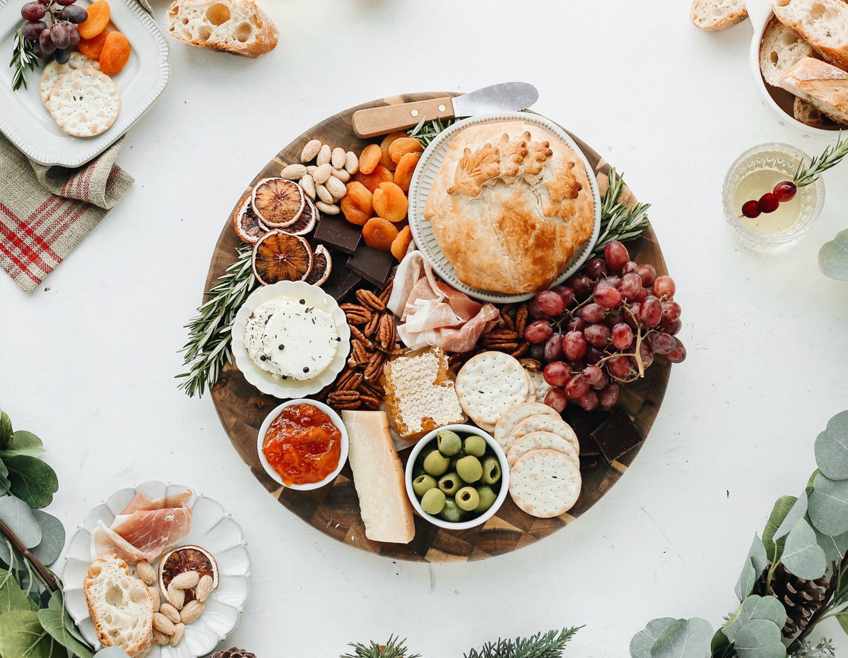 Camille Styles showcases a baked brie cheese board with chocolate, dried fruits, crackers, and grapes.