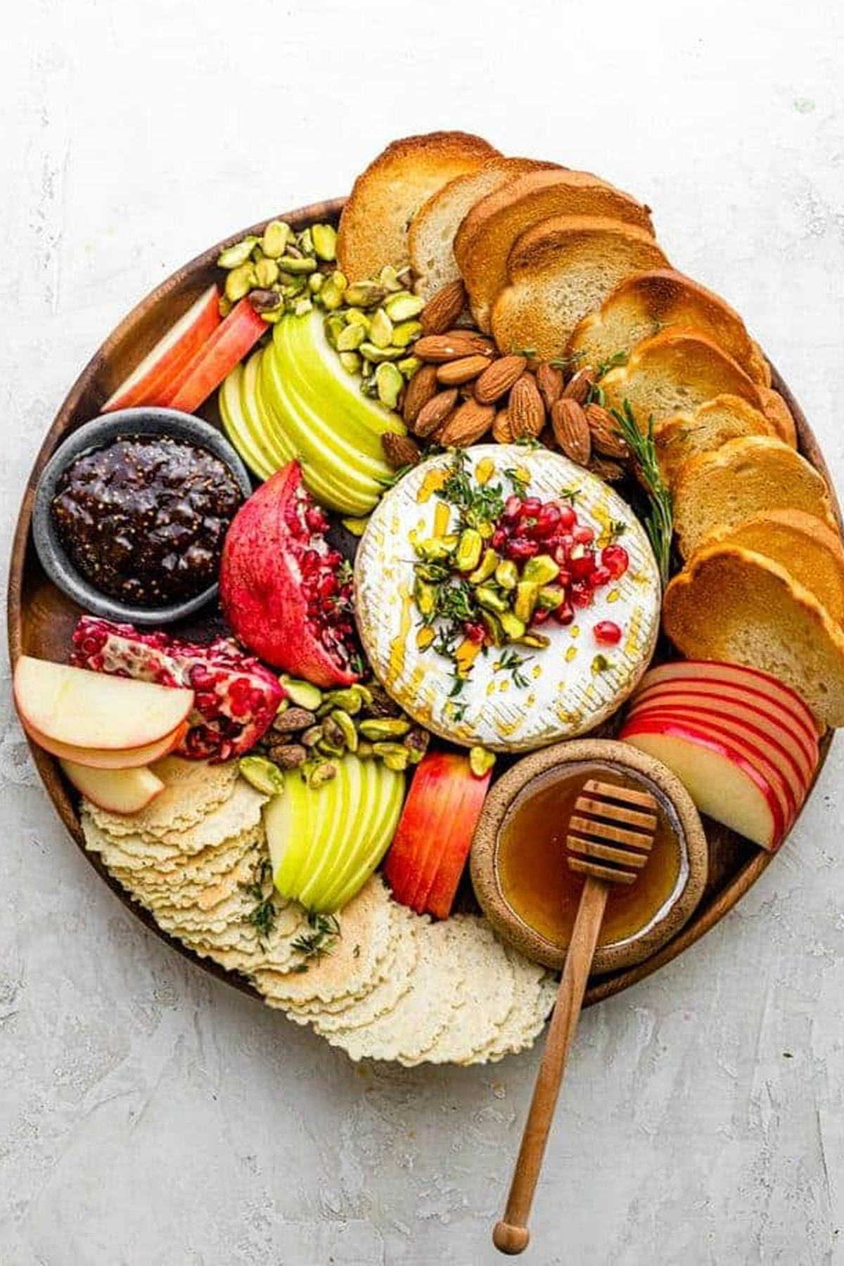 Feel Good Foodie includes, apples, honey, almonds, pomegranates, bread, and a baked brie ball on their charcuterie board.
