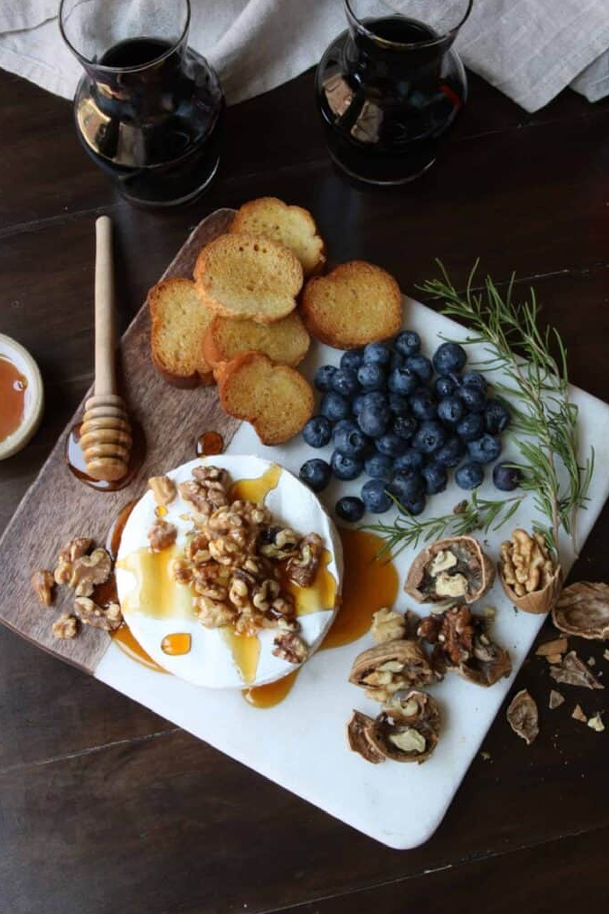 Brie cheese, honey, berries, and bread are shown on Kindly Sweets warm brie charcuterie board.