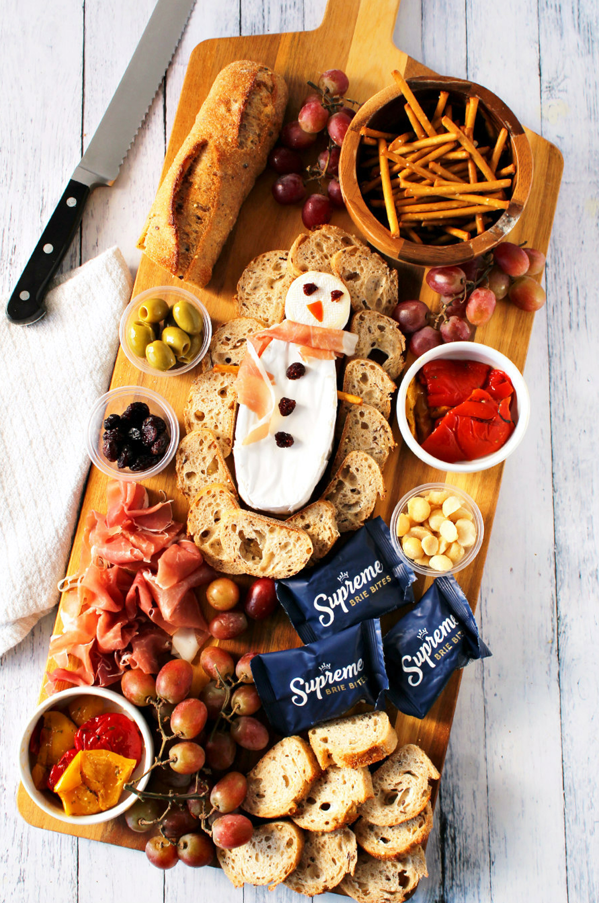 A brie snowman, pretzels, olives, grapes, and meat are included on Living La Vida Holoka's brie cheese board.