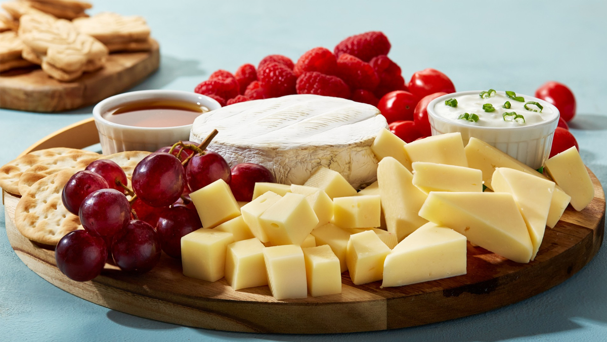 Dairy Farmers of Canada maple charcuterie board shows tomatoes, raspberries, grapes, crackers, and cheese.