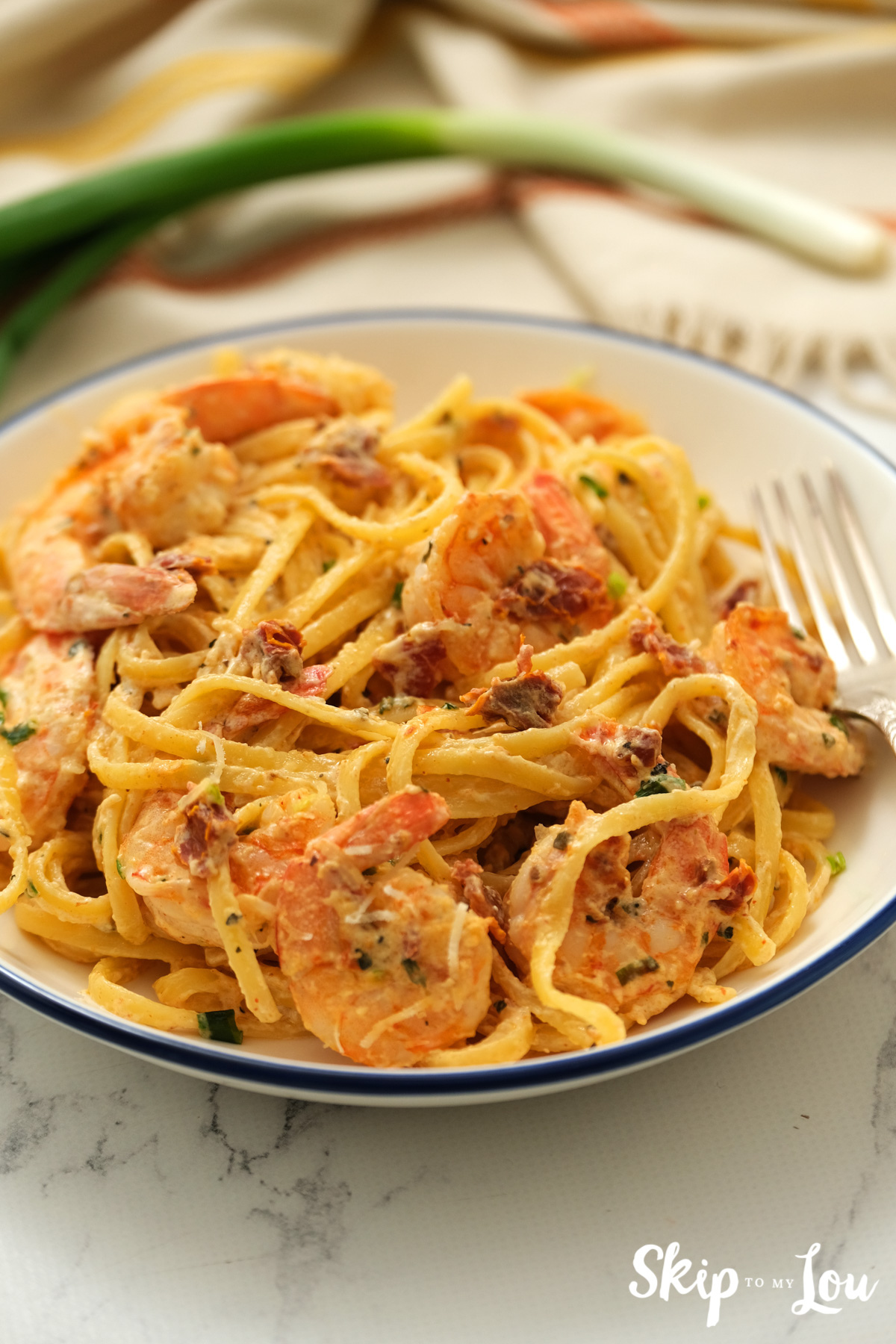 Blue-rimmed bowl with a serving of Cajun shrimp pasta, by Skip to my Lou.