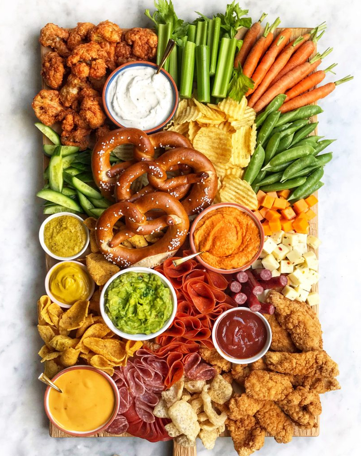 The Delicious Life's board is full of chips, veggies, meats, cheese, pretzels. and dips.