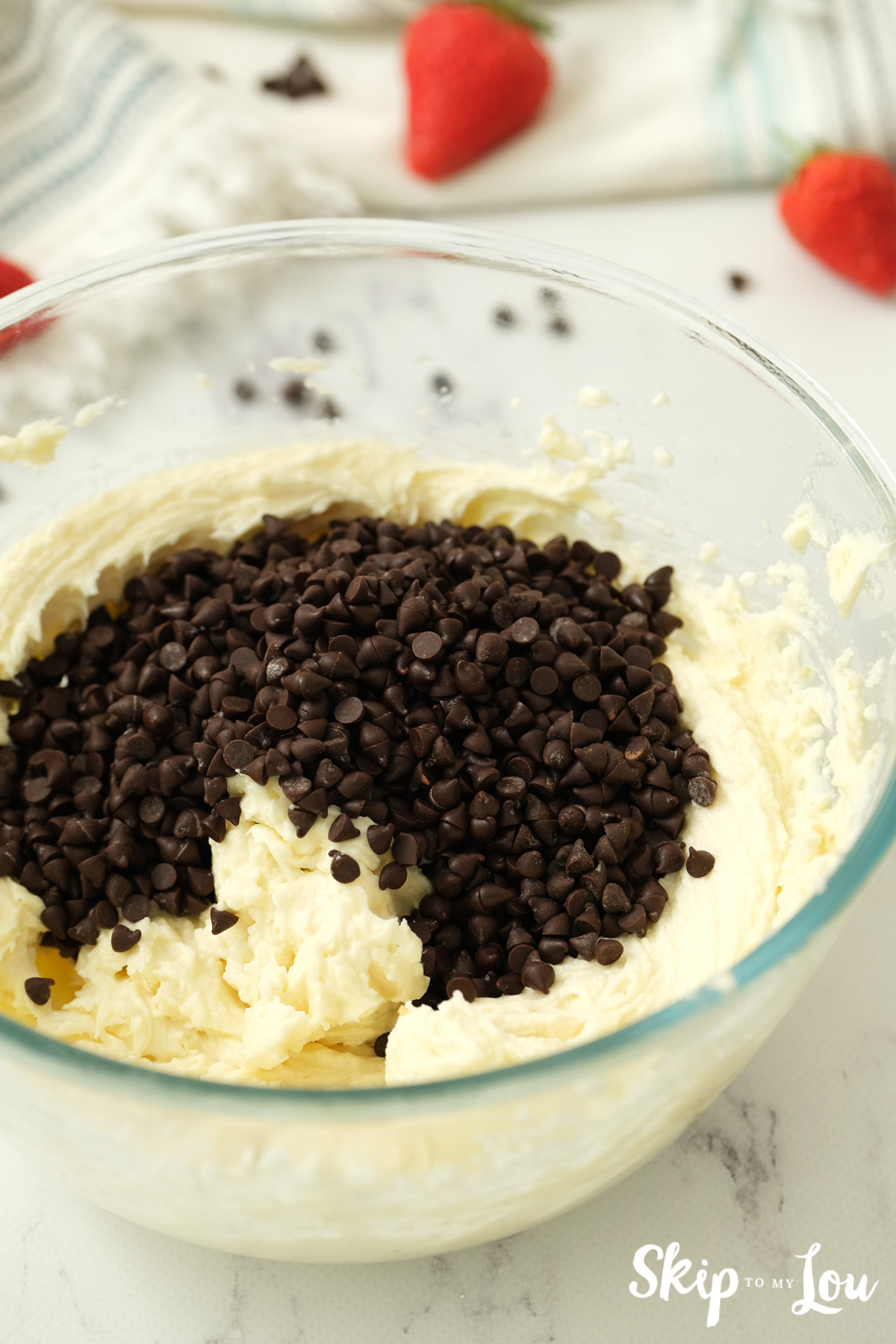 Chocolate chips sitting on top of a mixture of butter, powdered sugar, cream cheese and brown sugar, by Skip to my Lou.