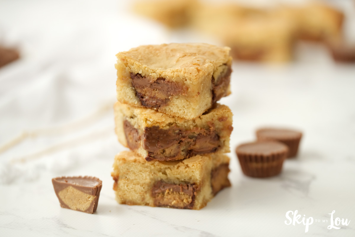 Three peanut butter cup blondies stacked on the countertop, by Skip to my Lou.