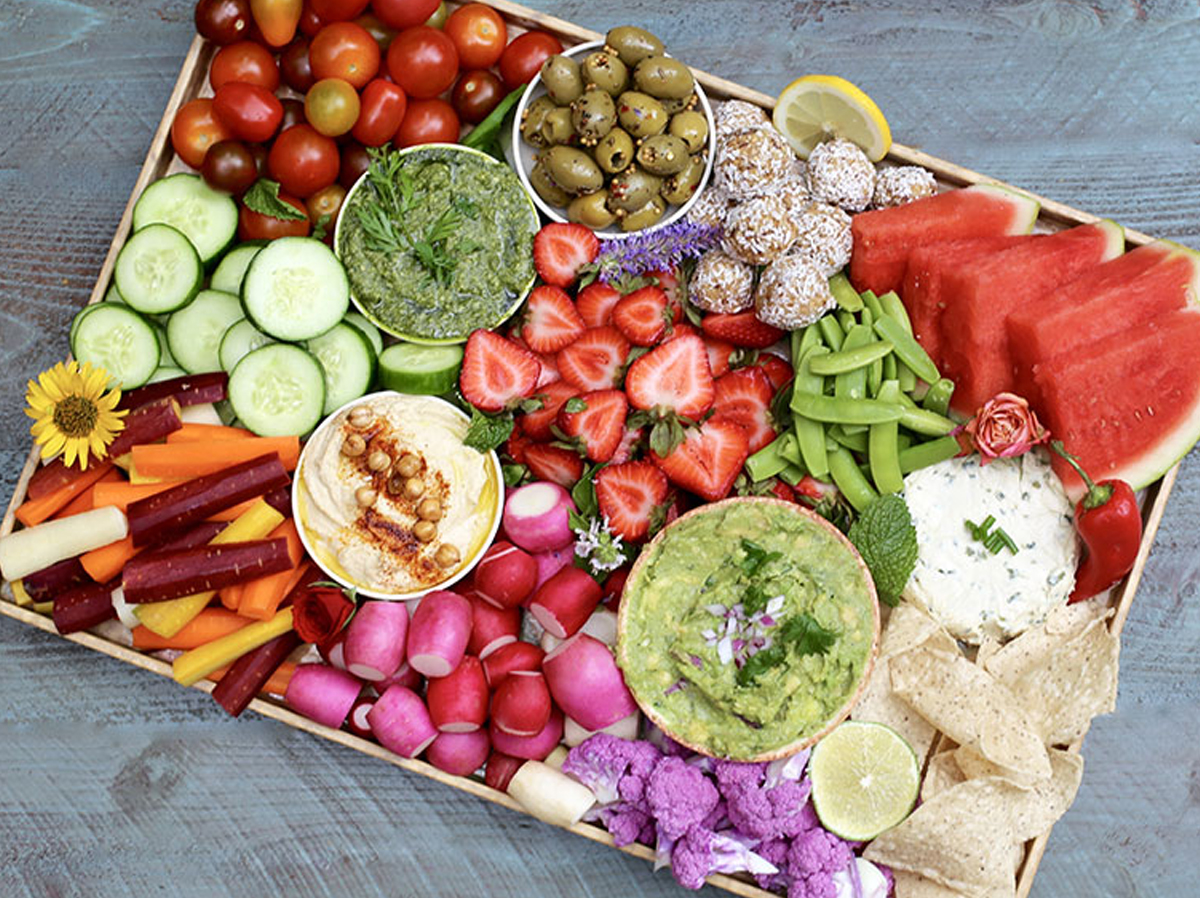 Elise museles rainbow charcuterie board idea includes a mix of veggies, fruits, and dips.