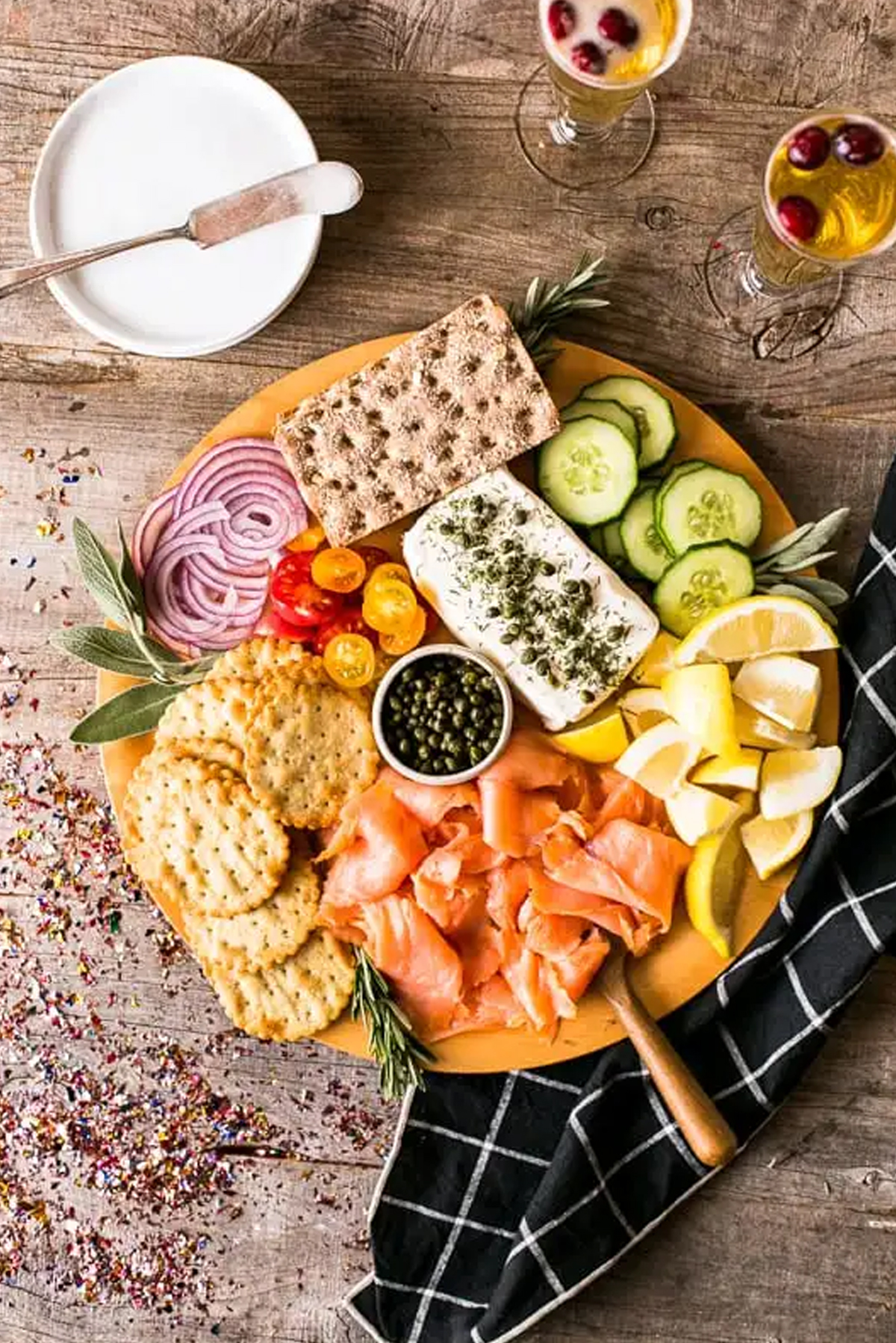 Cream Cheese, cucumber slices, onion, salmon, and crackers is presented on Kimbrough Daniels board.