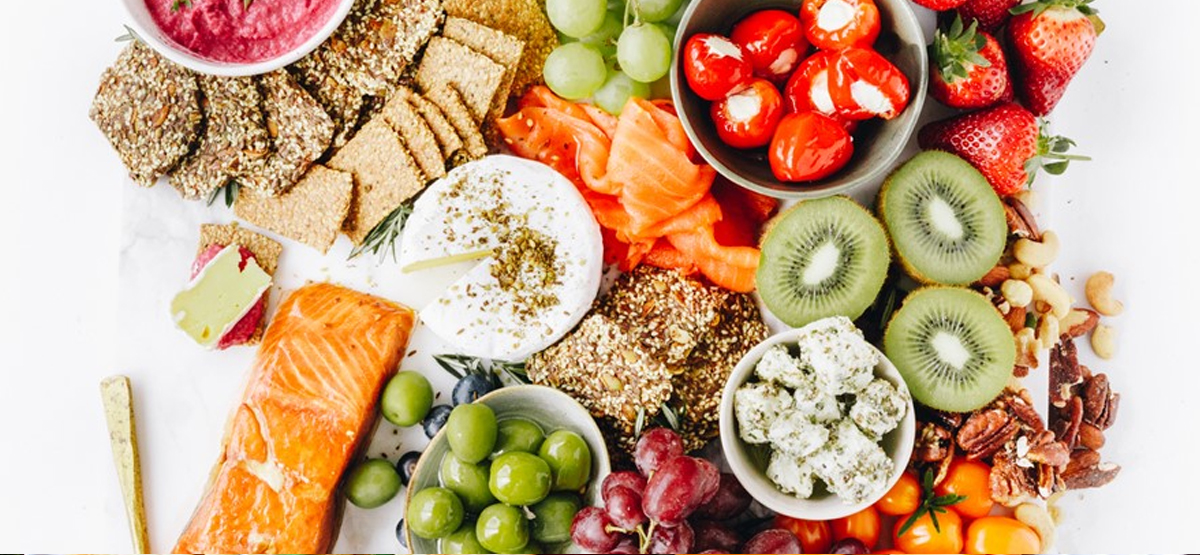 Crackers, kiwi, salmon, grapes, strawberries, and hummus are presented on Regal Salmon's board.