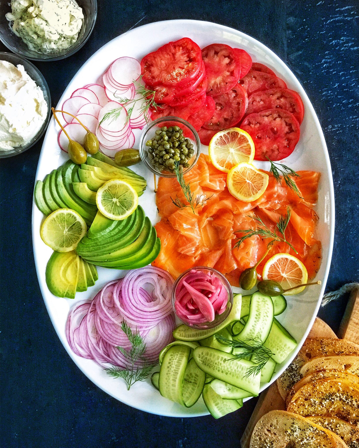 The Delicious Life displays salmon, tomato, lemons, avocado, and onions, on their charcuterie board.