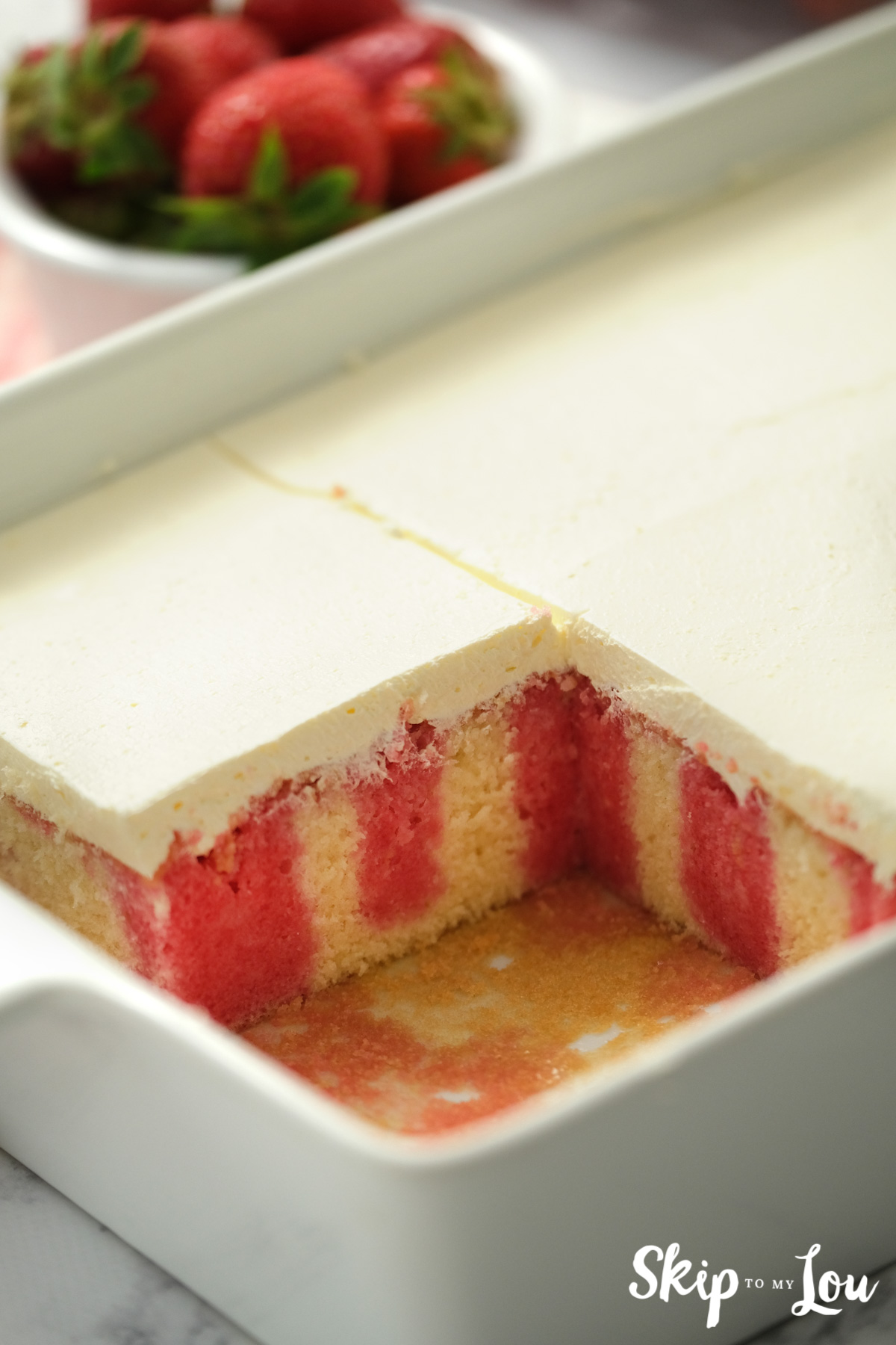 Strawberry poke baked in a pan, iced with smooth white icing, by Skip to my Lou.