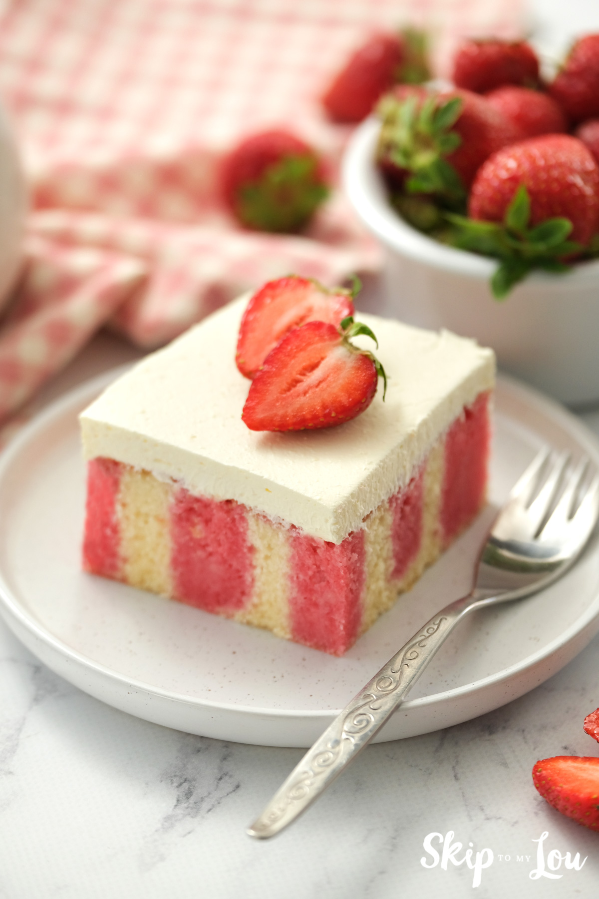 One serving of strawberry poke cake with a fresh sliced strawberry on top, by Skip to my Lou.