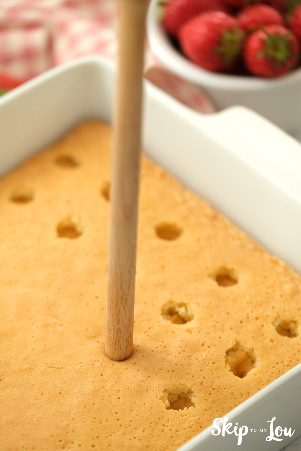 Wooden spoon handle poking holes in the top of a baked cake, by Skip to my Lou.