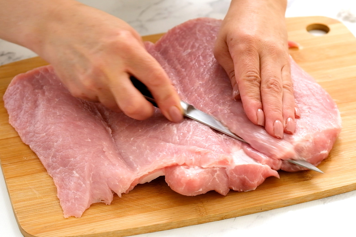 Pork loin on a wooden cutting board being butterflied, by Skip to my Lou