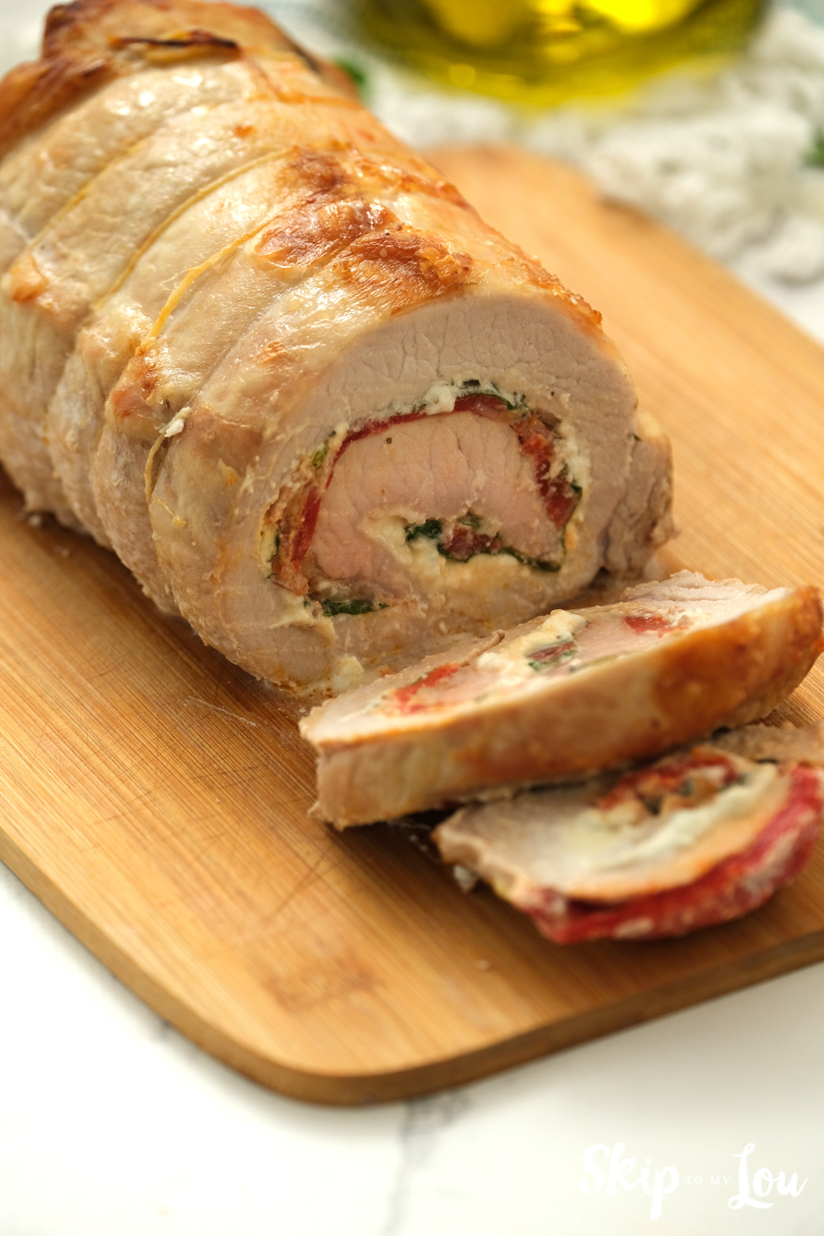 Stuffed pork loin resting on a wooden cutting board, by Skip to my Lou.