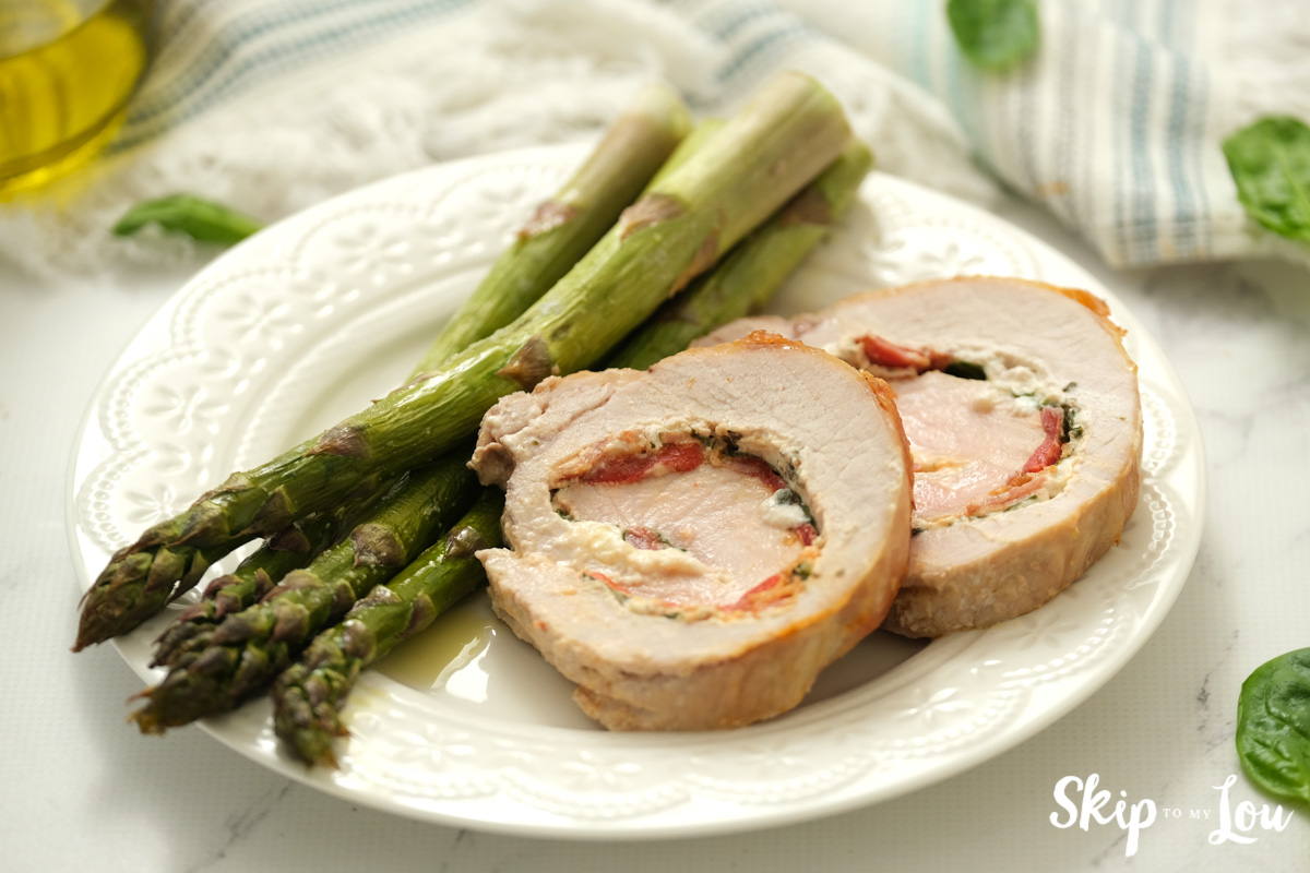 Roasted asparagus and stuffed pork loin on a white dinner plate, by Skip to my Lou.