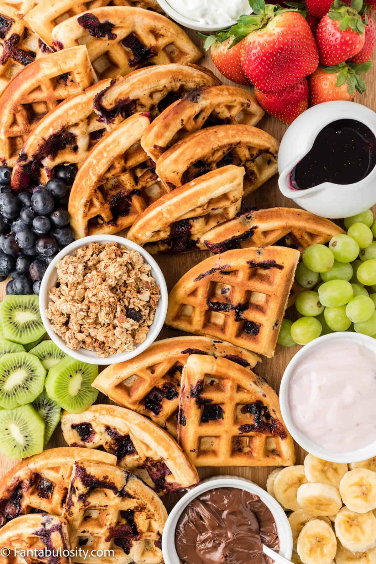 bluerberry waffles take center stage surrounded by fruit and jam on this board from fantabulosity.