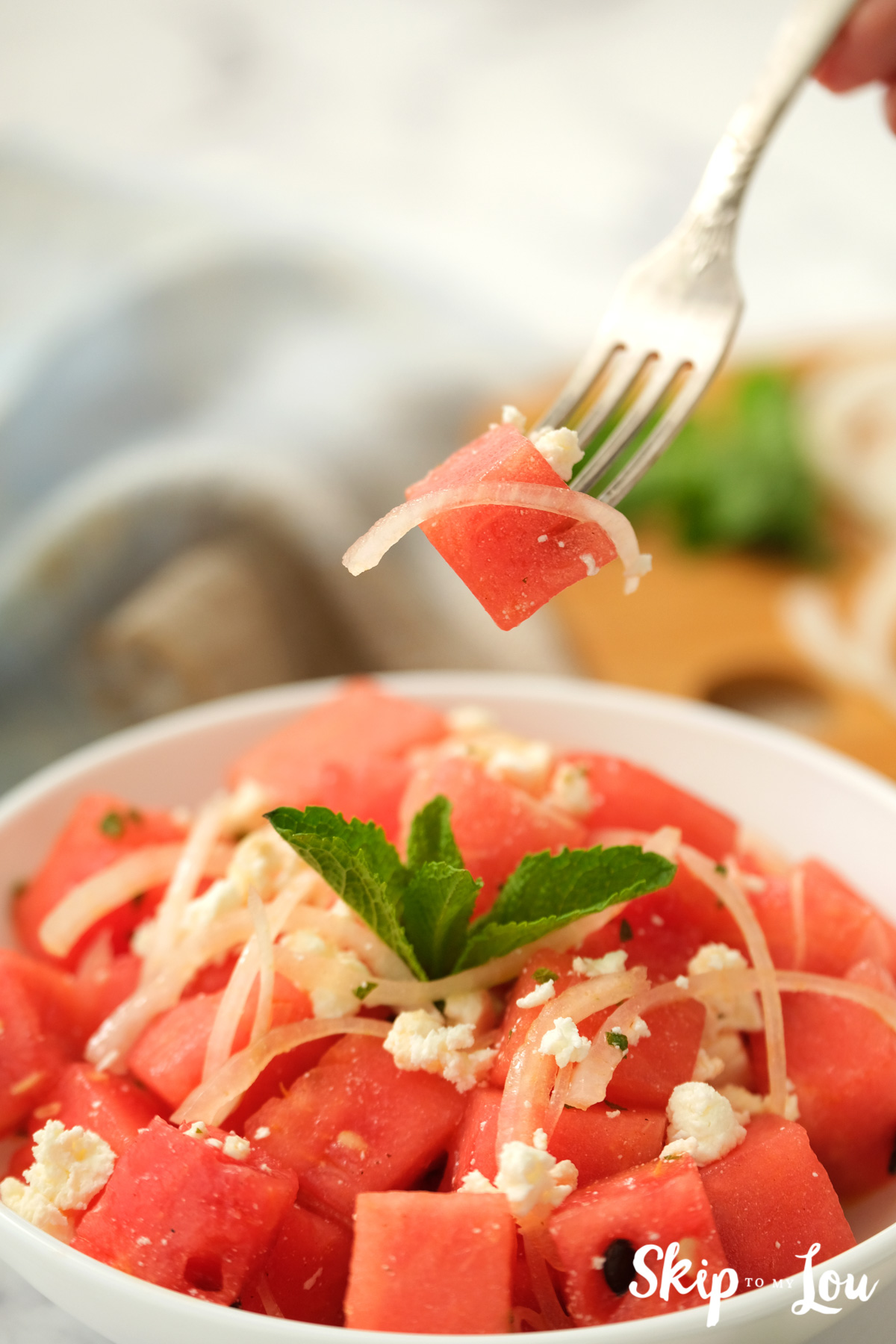 Silver fork holding a bite of Watermelon Salad, by Skip to my Lou.