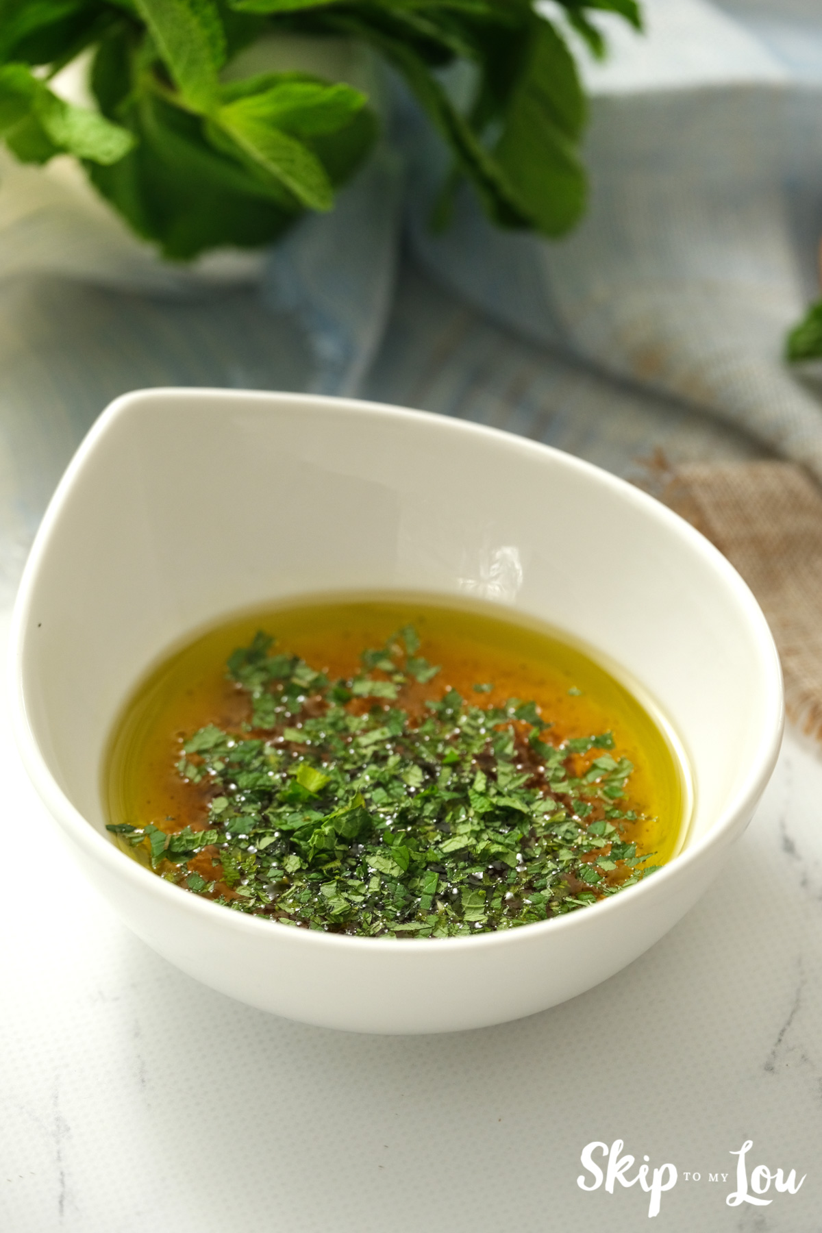 Freshly chopped herbs and olive oil in a white bowl, by Skip to my Lou.