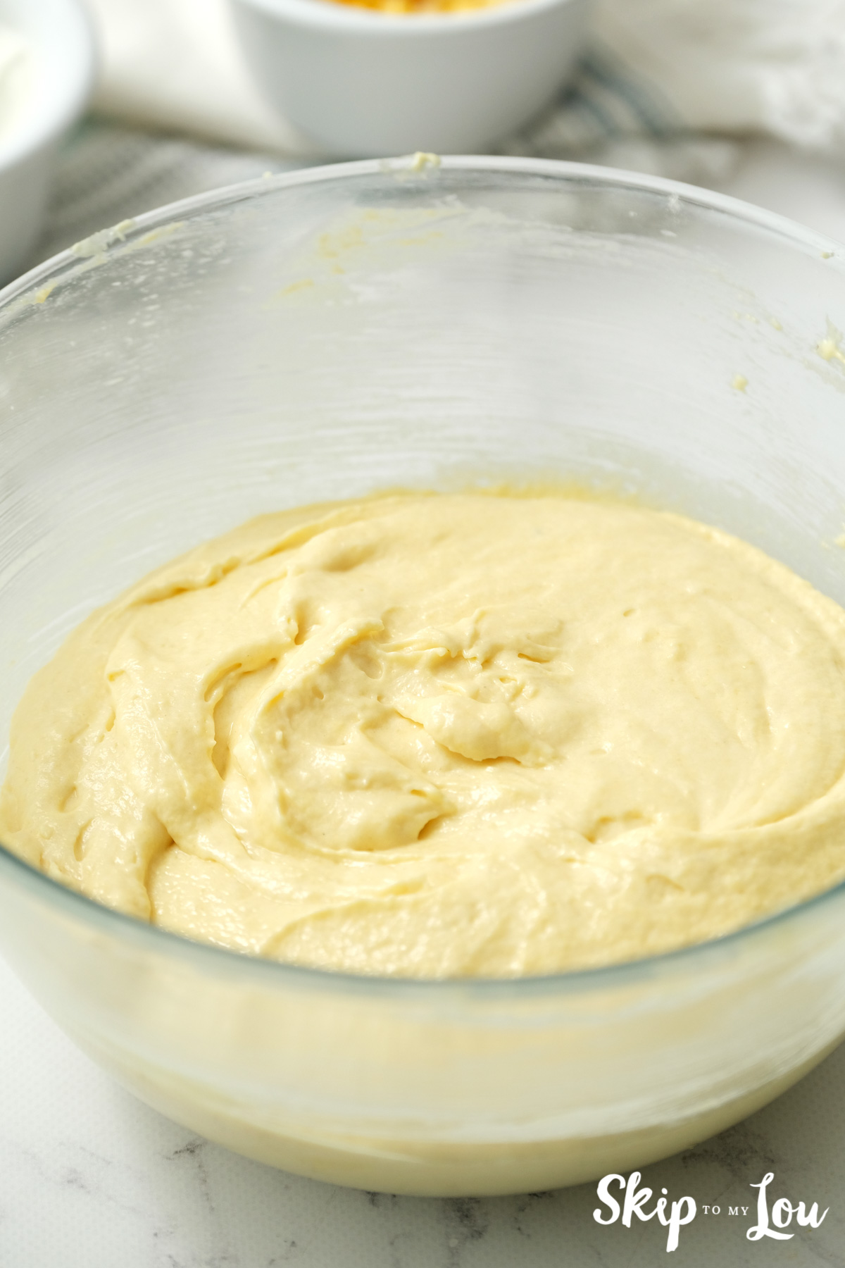 Wet ingredients for cornbread whisked together in a clear glass bowl, by Skip to my Lou.