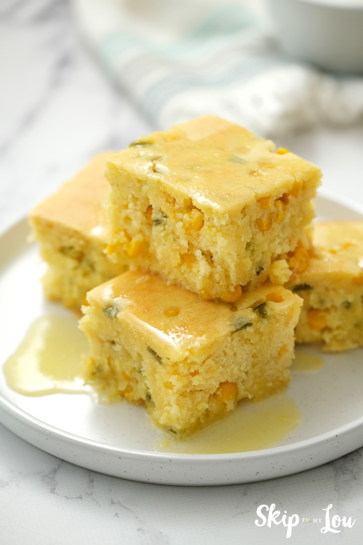 Four square pieces of World's Best Cornbread stacked on a white plate, by Skip to my Lou.