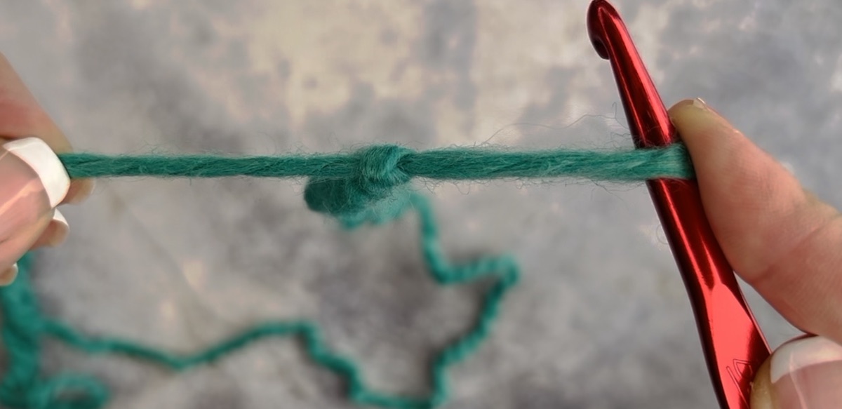 How to make a slip knot using a crochet hook, step 3, pull the hook and hold the other end of the yarn at the same time