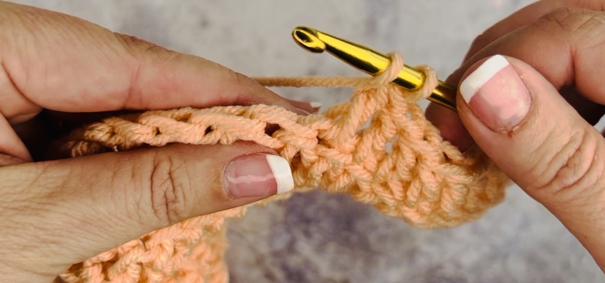 Second step to do a double crochet with salmon-colored yarn.