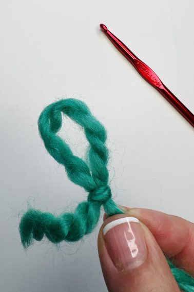 How to make a slip knot, final step, a pair of hands holding a green yarn slip knot