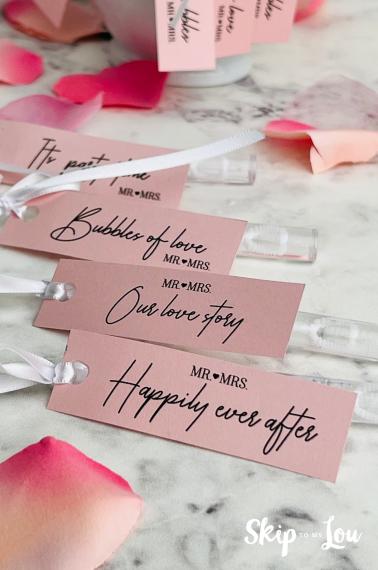 Bubble party favor tags with text such as "happily ever after" on pink paper, on top of a white marble background.
