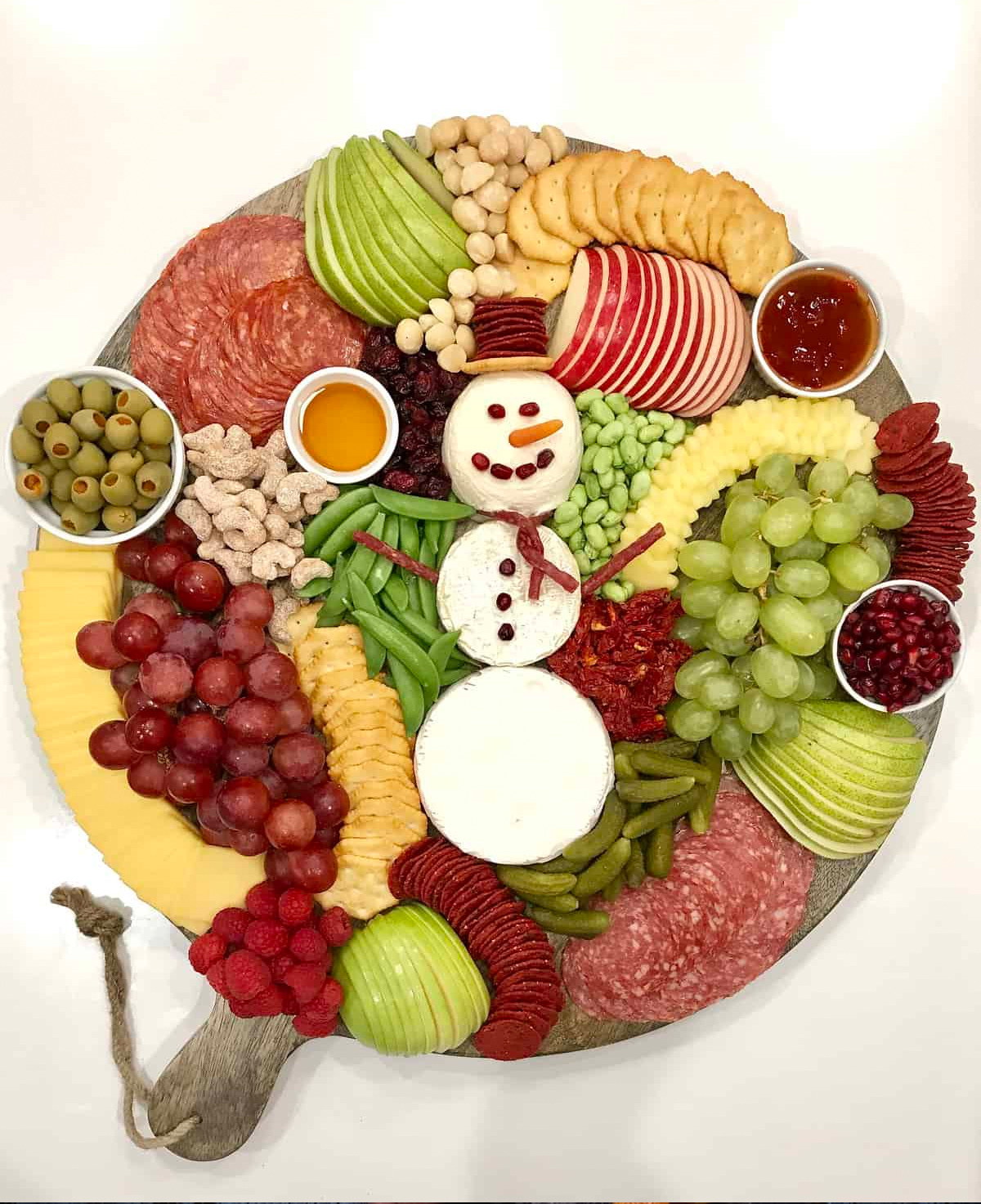 The BakerMama's Snowman snack board is filled with pears, apples, cheese, meat, olives, crackers, and nuts.