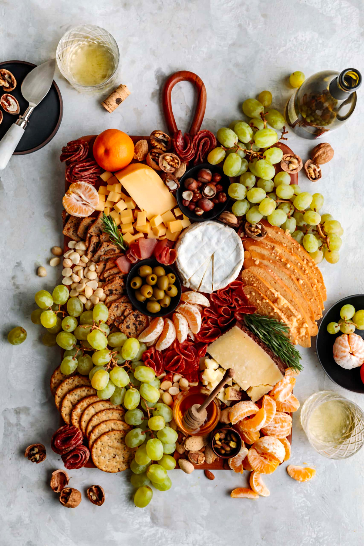 Yoga of Cooking's charcuterie board features an array of hard and soft cheeses, seasonal fruits like clementines, and a touch of fresh rosemary sprigs