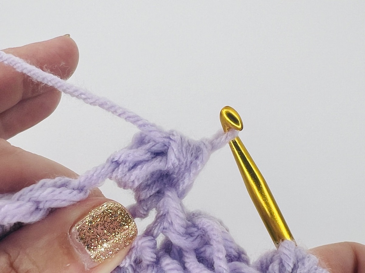 Crocheting a bobble stitch with one loop left on a gold hook of purple yarn.