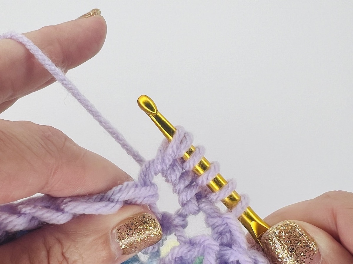 Crocheting a bobble stitch with six loops on a gold hook of purple yarn.