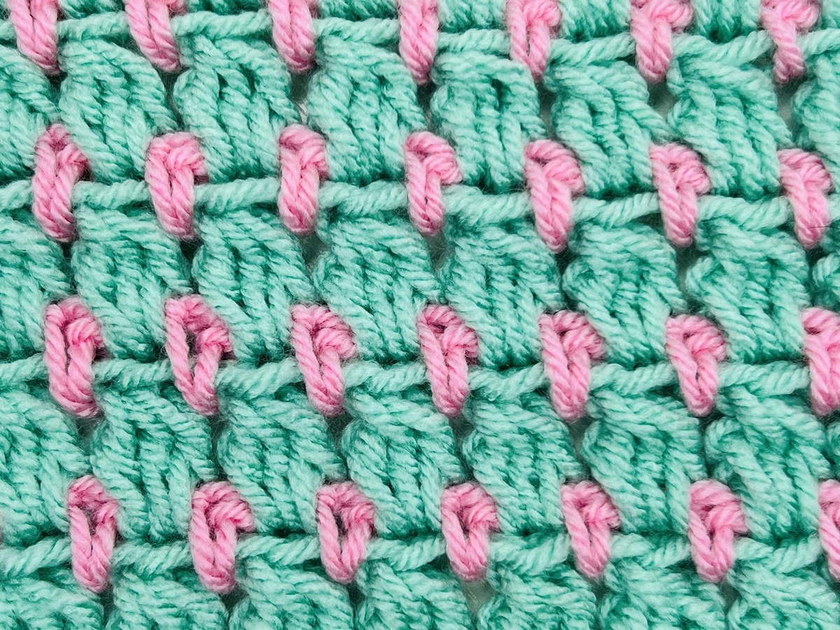 A mint green and light pink swatch of cluster crochet stitching on a white background.