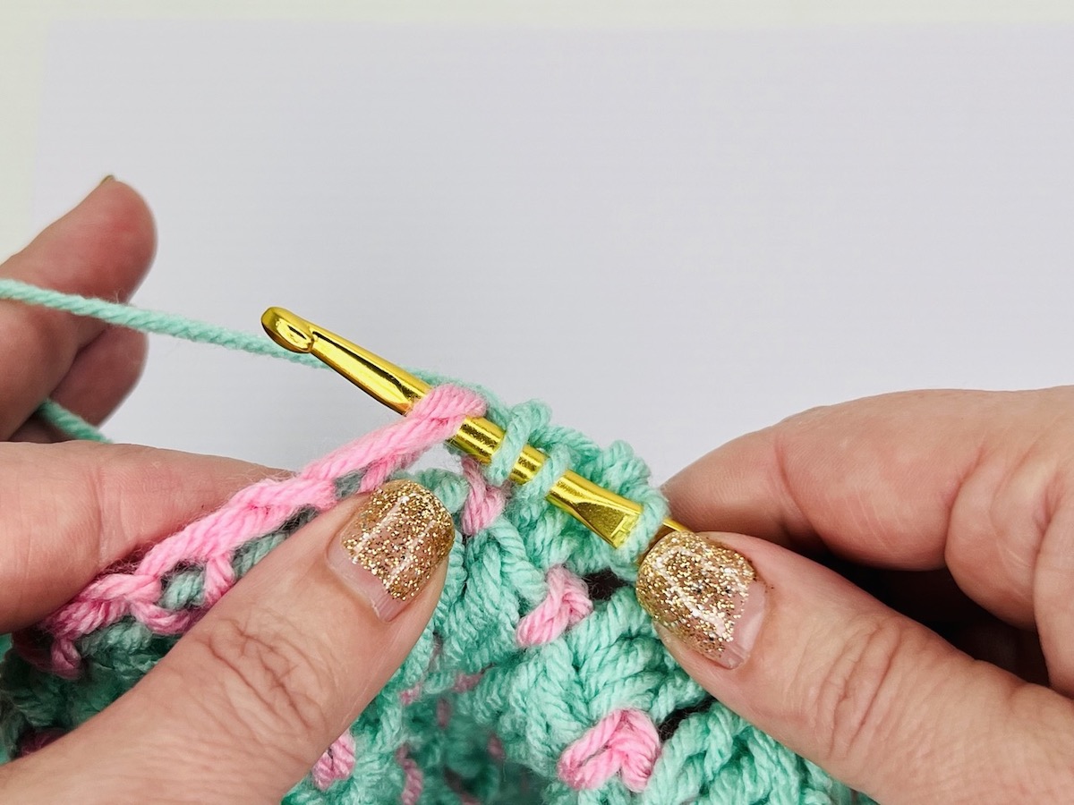 Mint green and light pink crochet piece made of cluster stitches on a white background.