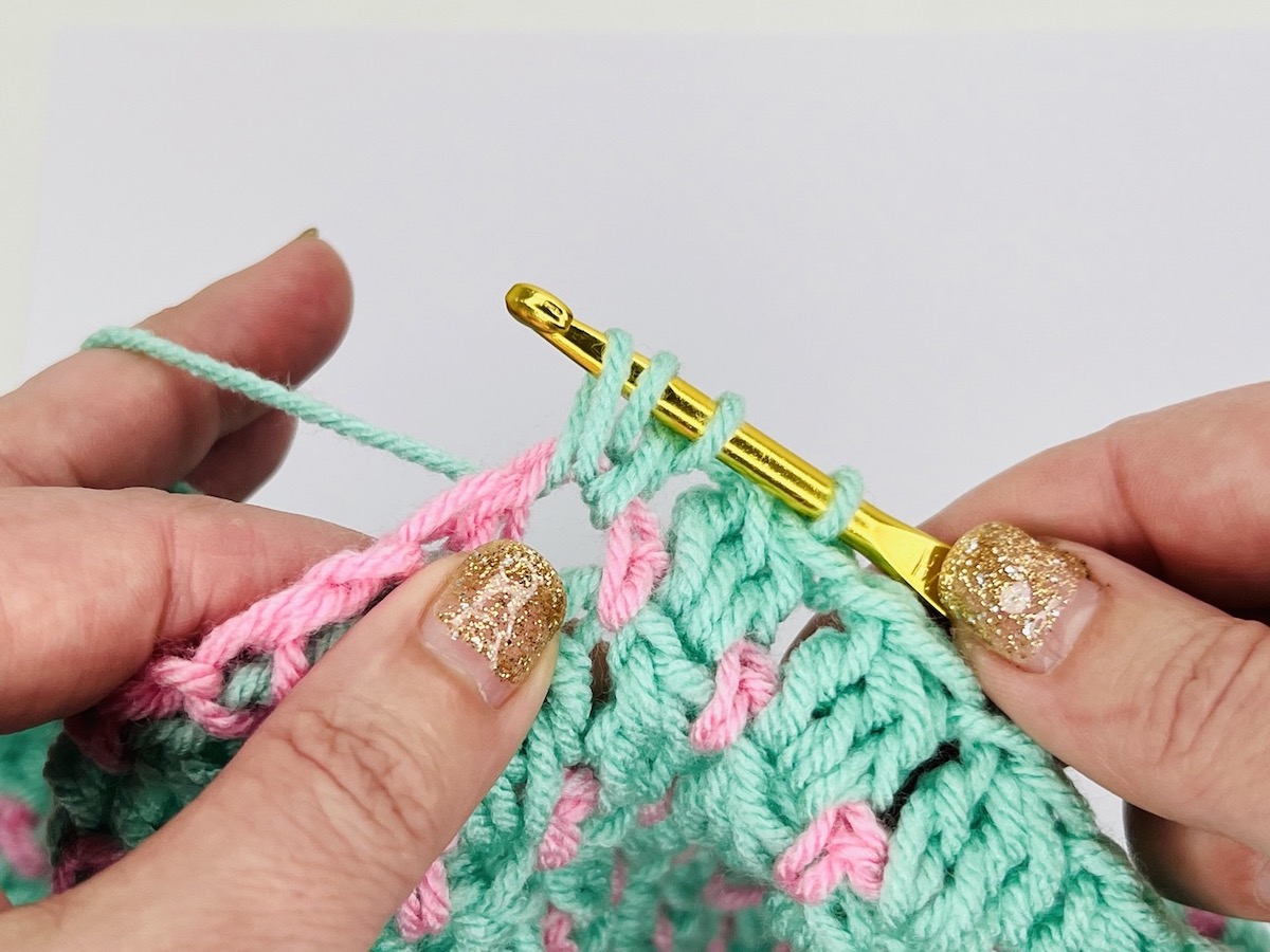 Mint green and light pink yarn swatch of cluster stitches on a white background.