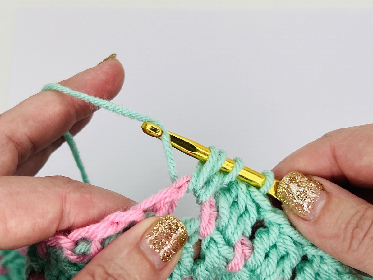 Cluster stitch being completed in mint green over a row of light pink singe crochet row.