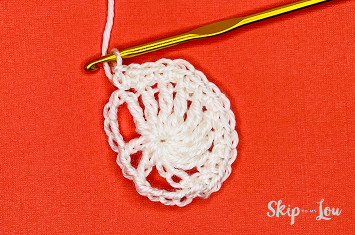 White yarn crocheted into a circle with holes for eyes and a nose of a skull on an orange background.