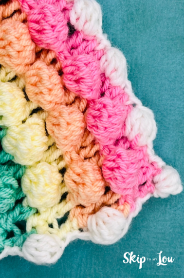 Image shows a finished bobble stitch border crochet project made with pink, orange, yellow, green and white yarn. Tutorial is from Skip to my Lou