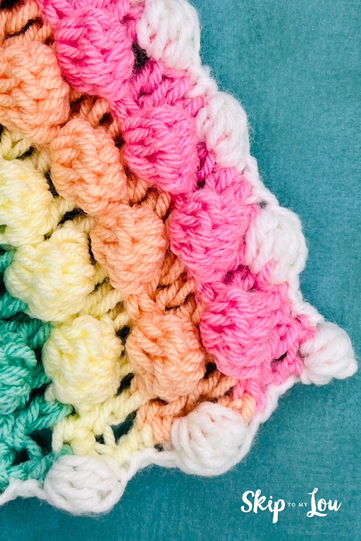 Image shows a finished bobble stitch border crochet project made with pink, orange, yellow, green and white yarn. Tutorial is from Skip to my Lou