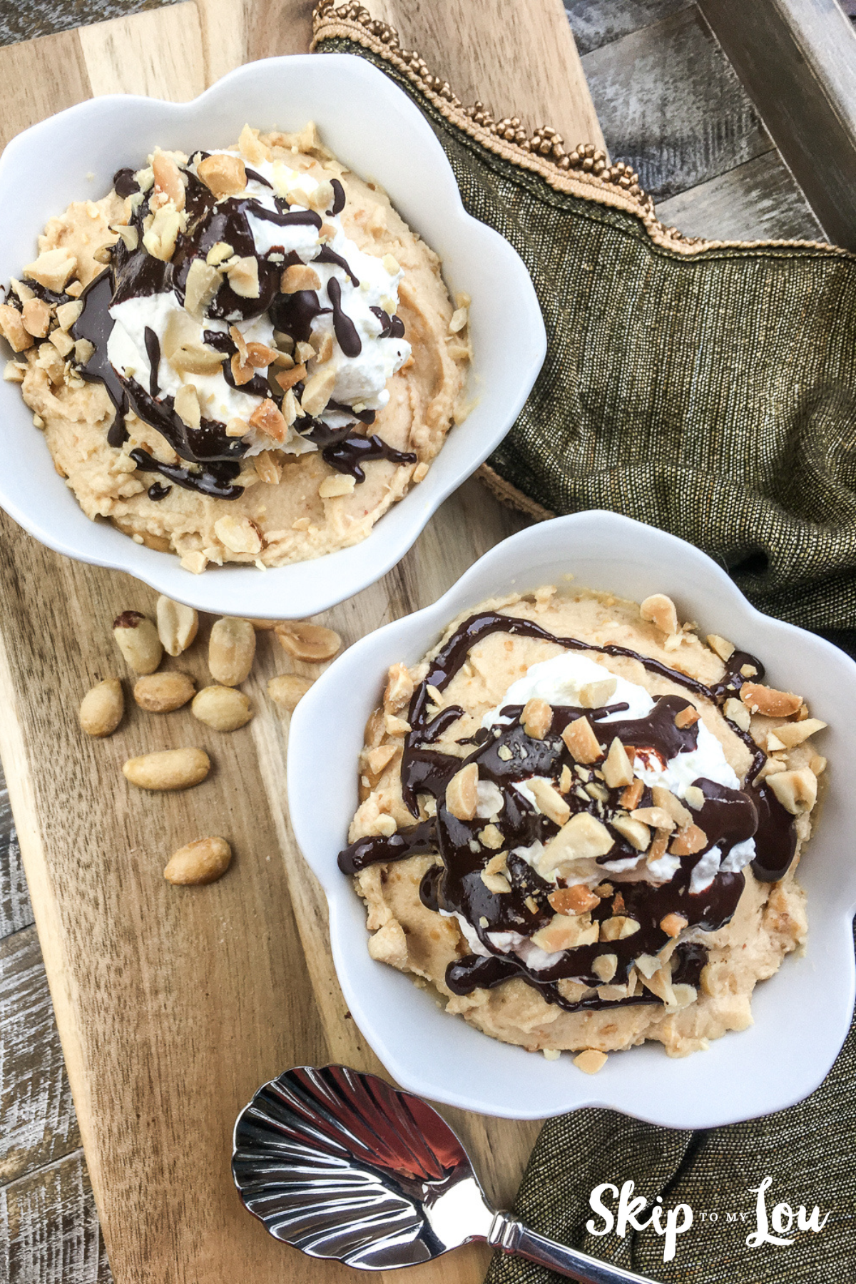 Image shows two bowls with chocolate peanut butter mousse parfait on top of a wooden board and a spoon next to it. There are loose peanuts on the table.