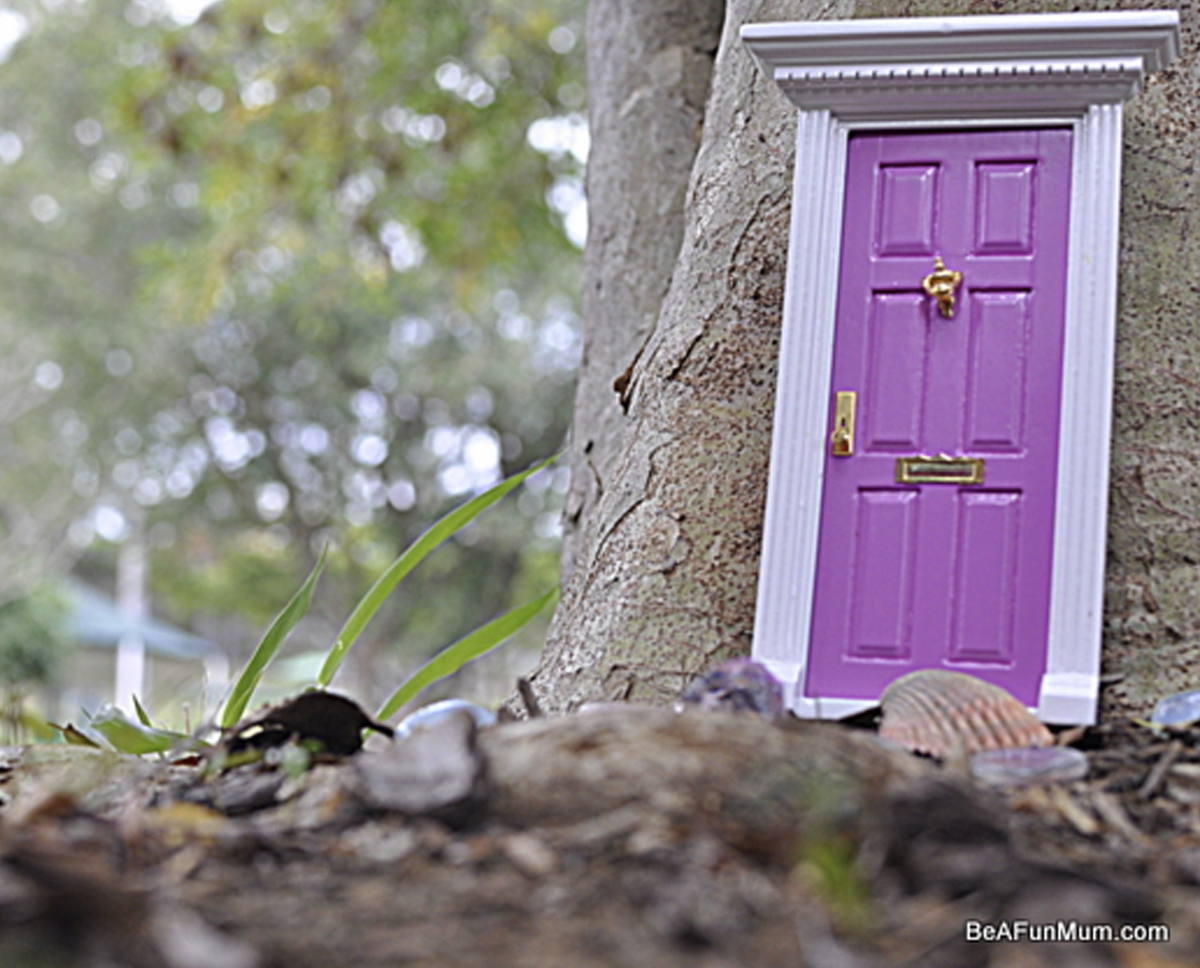 An ornate purple and white door placed against a tree truck to look like an entrance to a fairy home. 
