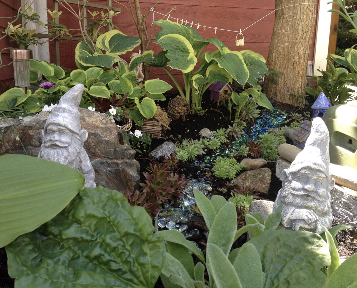 A large fairy garden guarded by two garden gnomes. The garden includes various plants and some rocks. 