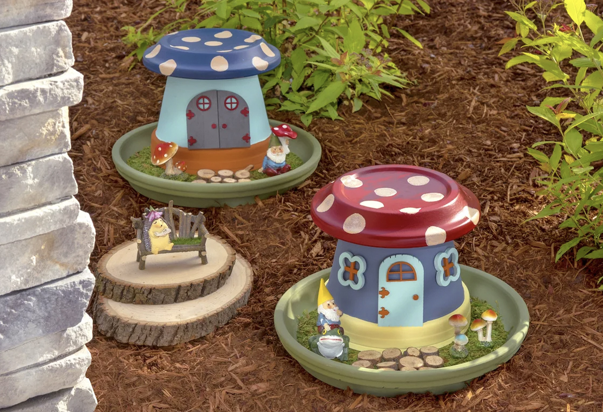 Two small toadstool houses in small ceramic plates The houses belong to two gnomes who are both sitting in their gardens outside.