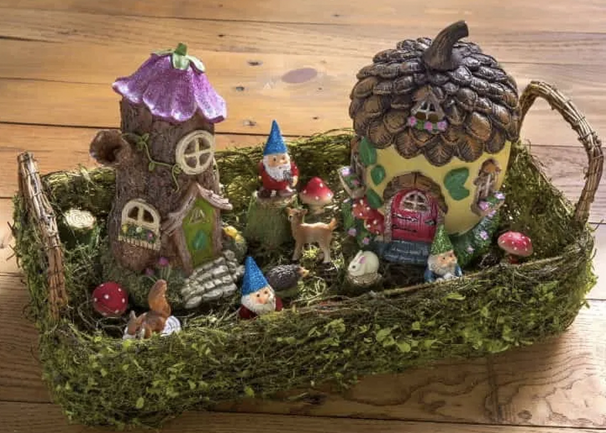 A fairy garden made in an old wicker basket. This includes two small gnome houses, toadstools, and various animals such as a squirrel, deer, and rabbit. 