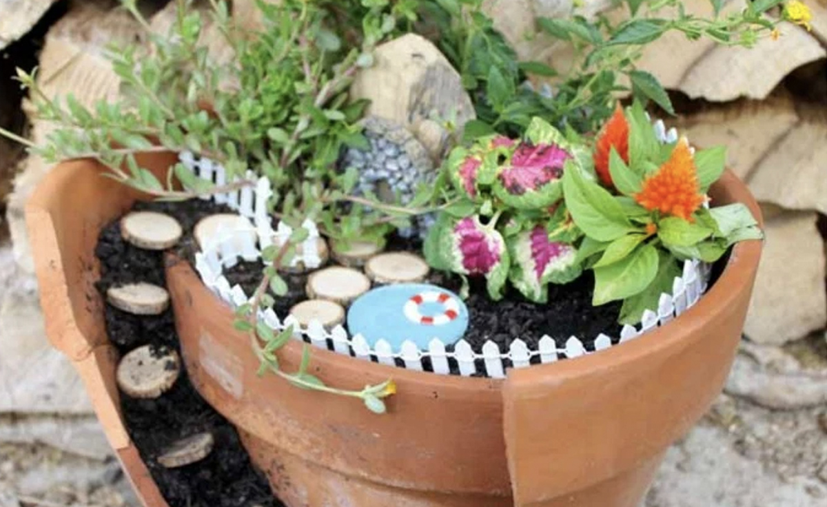 A fairy garden that's predominately made up of plants. It does include a fence around the layered pots as well as a pool made from blue paint.