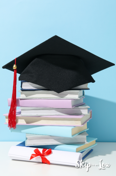 Image shows a black graduation cap on top of a stack of untitled books, and the background is light blue.