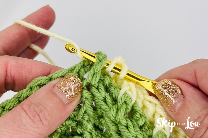 Yellow yarn is being pulled up on a gold hook to create a waffle stitch.