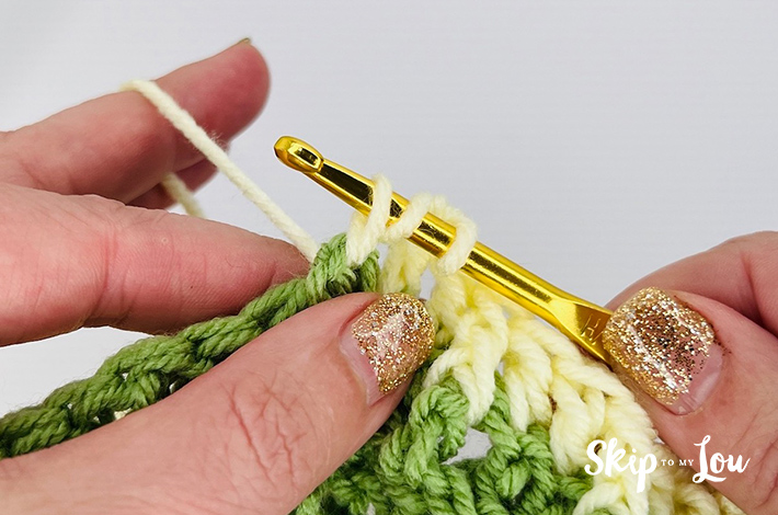 Yellow yarn is being pulled up on a gold hook to create a waffle stitch.